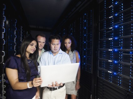 Business people looking at laptop in server room