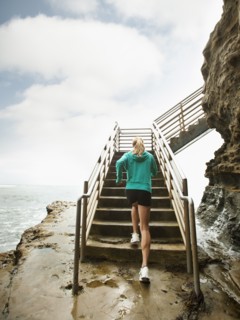 Caucasian woman running up stairs next to ocean