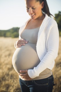 Pregnant Hispanic mother holding stomach in field