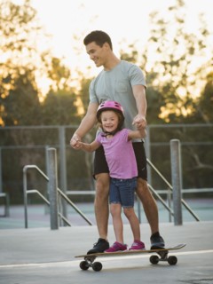 Father and daughter riding skateboard in park