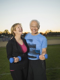 Older couple lifting weights together in urban park