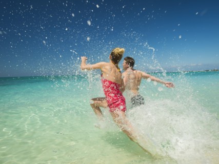 Caucasian couple splashing in waves in tropical ocean