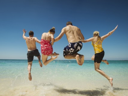 Caucasian couples jumping for joy in water on tropical beach