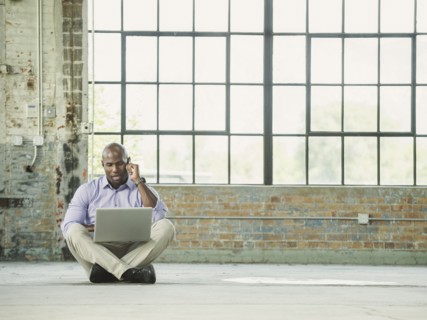 Black businessman using laptop and cell phone on warehouse floor