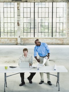 Businessmen reading blueprints in empty warehouse