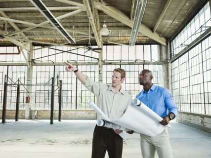 Businessmen reading blueprints in empty warehouse