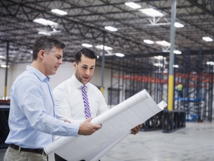 Caucasian architects reading blueprints in warehouse