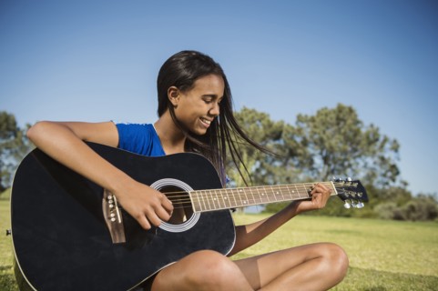Mixed race girl playing guitar in park