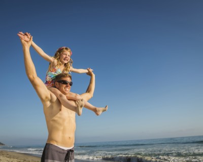 Caucasian father carrying daughter on beach