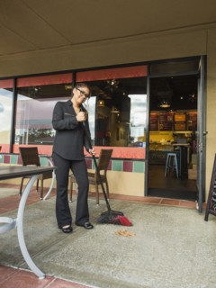 Hispanic business owner sweeping sidewalk