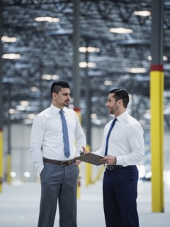 Businessmen with clipboard talking in empty warehouse