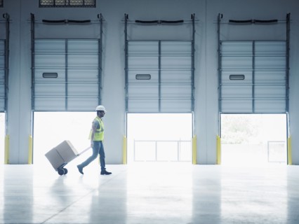 Indian worker pulling hand truck near open loading dock doors