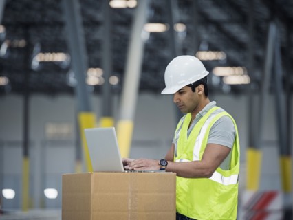 Indian worker using laptop on cardboard box in warehouse