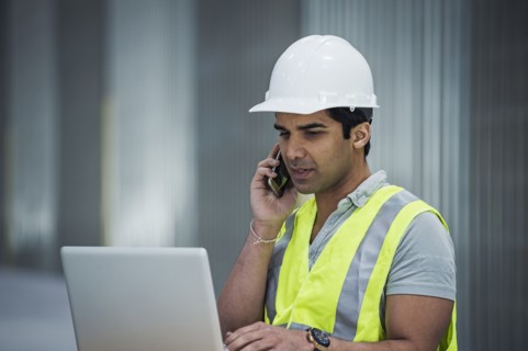 Indian worker using laptop and cell phone in warehouse
