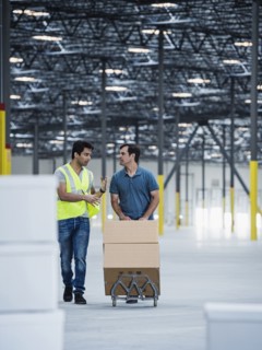 Workers pushing cardboard boxes on hand truck in warehouse