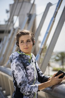 Caucasian woman leaning on bridge railing listening to earbuds