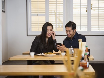 Smiling Chinese couple listening to cell phone in restaurant