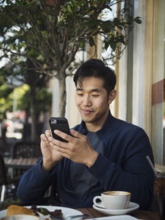 Smiling Chinese man texting on cell phone at outdoor cafe