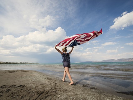 Caucasian girl walking with American flag at beach