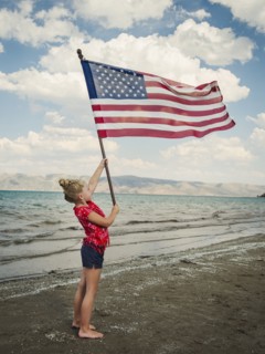Caucasian girl holding American flag at beach