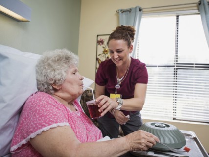 Caucasian nurse feeding patient in hospital bed