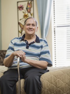 Smiling Caucasian man sitting on bed holding cane