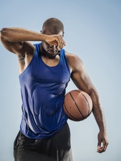 Black man holding basketball wiping sweat off forehead
