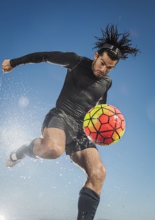 Water splashing on Hispanic man kicking soccer ball