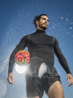 Water splashing on Hispanic man holding soccer ball