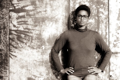 Serious African American woman leaning on rusty metal wall