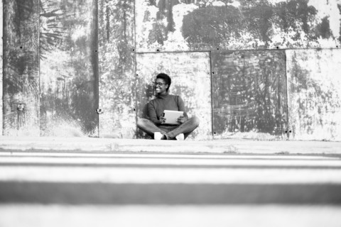 Distant African American woman sitting on ground using digital tablet