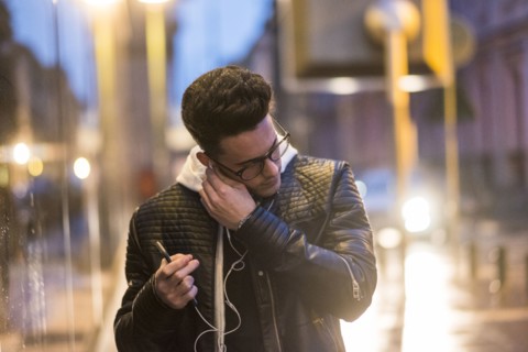 Caucasian man putting earbud in ear outdoors