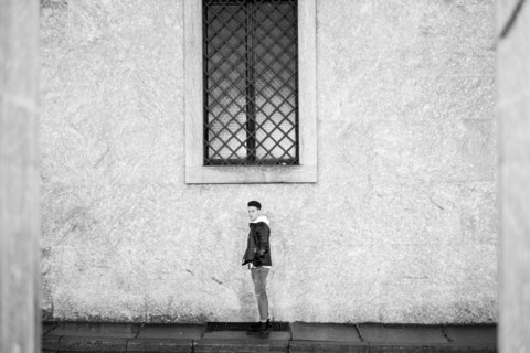 Portrait of distant man standing underneath window on sidewalk