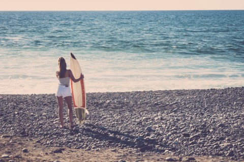 Caucasian woman standing on beach holding surfboard