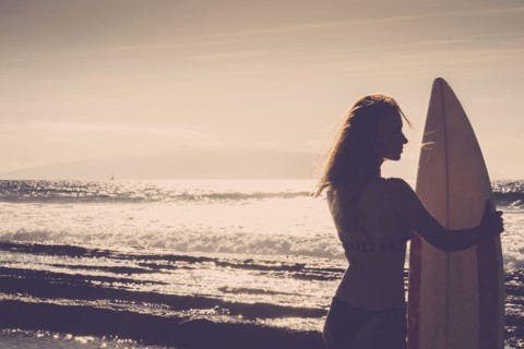 Caucasian woman standing on beach holding surfboard