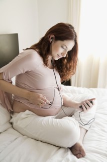 Pregnant Hispanic woman playing music for unborn baby