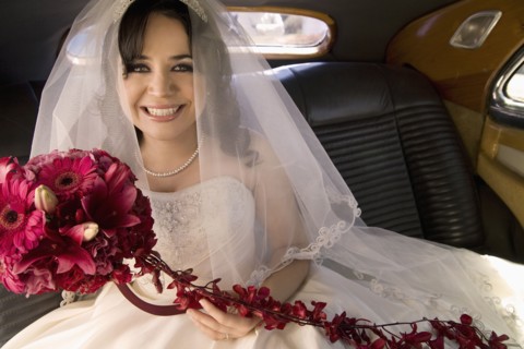 Hispanic bride sitting with bouquet in car