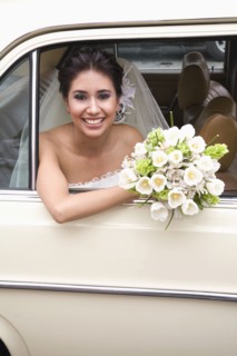 Hispanic bride sitting with bouquet in back of car