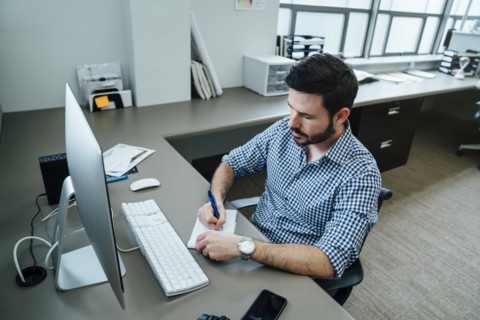 Caucasian businessman writing notes at a computer
