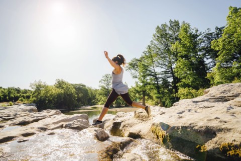 Caucasian woman jumping on rocks near river