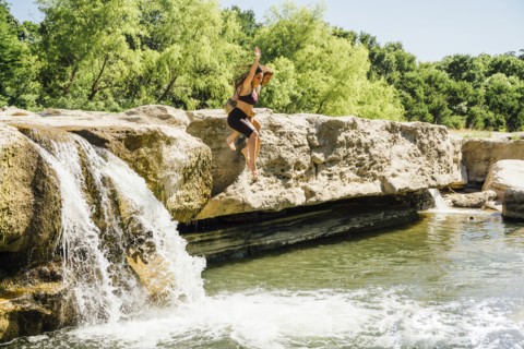 Caucasian couple jumping off rocks near waterfalls