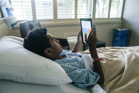 Black boy in hospital bed listening to digital tablet