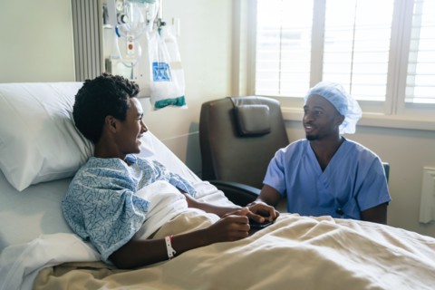 Black nurse talking to boy in hospital bed