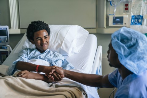 Black nurse shaking hands with boy in hospital bed