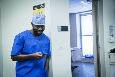 Smiling black nurse texting on cell phone