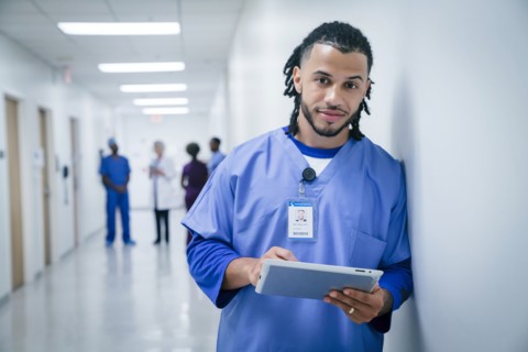 Smiling nurse leaning on wall in hospital using digital tablet