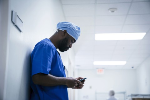 Black nurse leaning on wall texting on cell phone