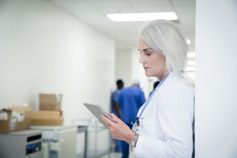 Caucasian doctor leaning on wall using digital tablet