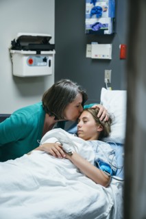 Mother kissing forehead of daughter in hospital bed