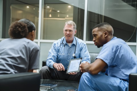 Doctor holding digital tablet talking to nurses in lobby